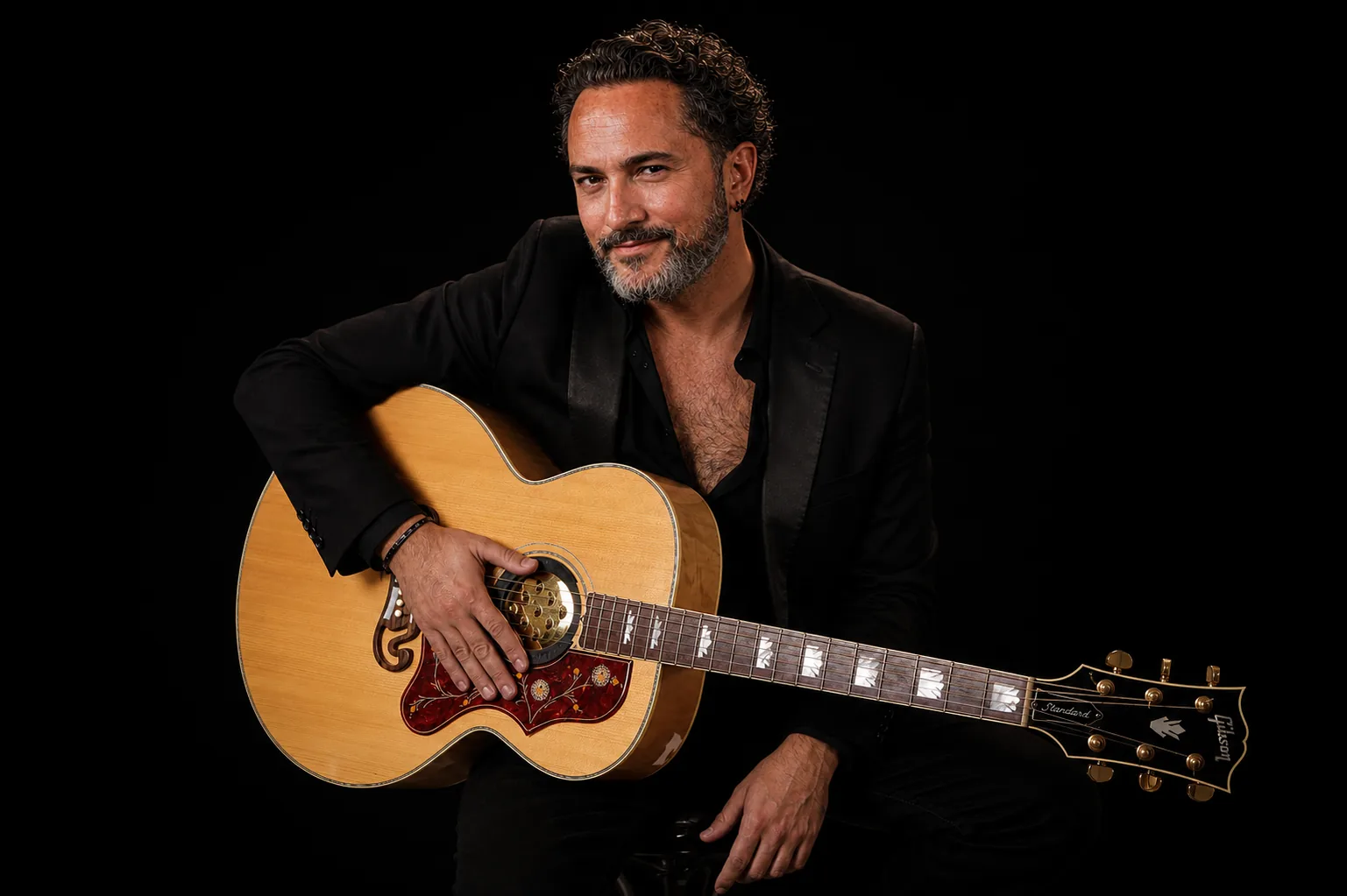Stefano Eliamo with an acoustic guitar on a black background